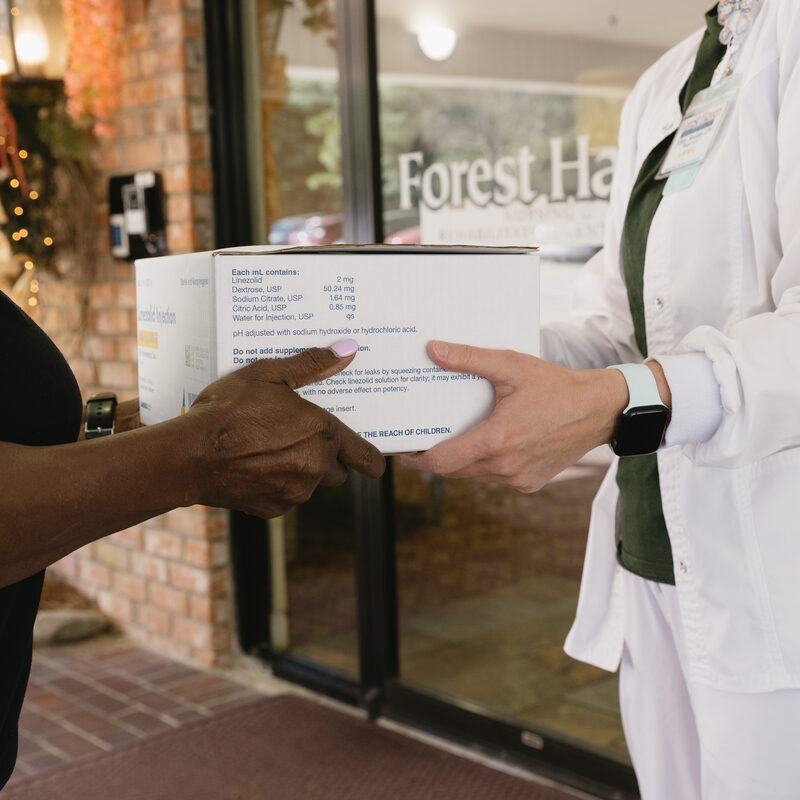 A Mitchell's Pharmacy team member delivering a box of medication to a patient at a care facility